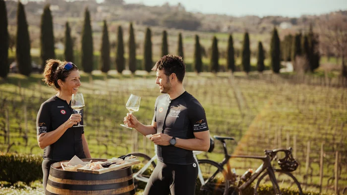 Due ciclisti che gustano vino e snack all'aperto vicino a una botte in vigneto