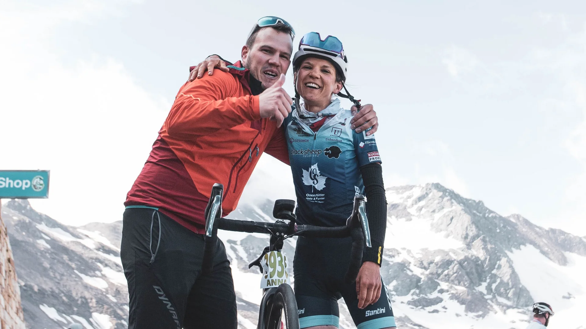 Cyclist with man in orange jacket posing near mountain after race