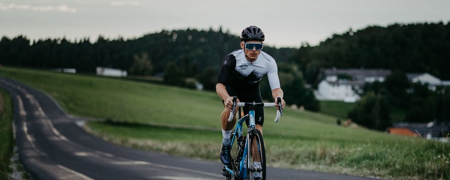 Ciclista in abbigliamento sportivo su strada di campagna con cielo nuvoloso