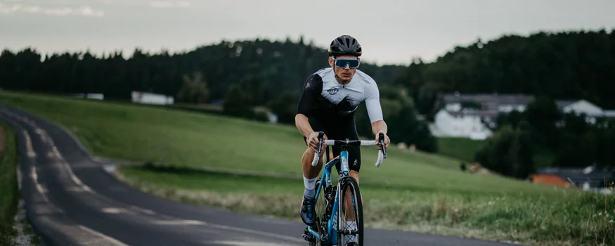 Ciclista in abbigliamento sportivo su strada di campagna con cielo nuvoloso
