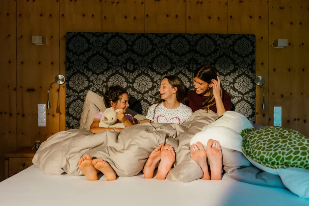 Mutter und zwei Kinder lachen zusammen im Bett mit Kuscheltier