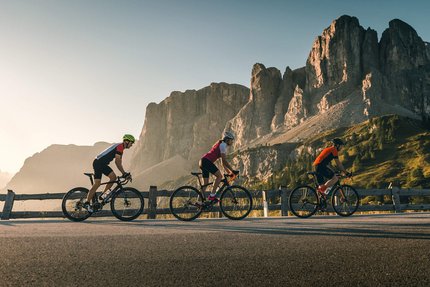 Three cyclists riding on mountain road with rocky cliffs behind