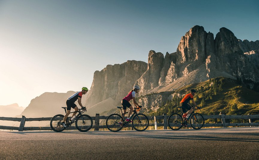 Three cyclists riding on mountain road with rocky cliffs behind