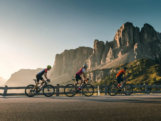 Warum Alta Badia auf jede Roadbike-Bucket-List gehört © Molography Drei Radfahrer fahren auf Bergstraße mit Felsen im Hintergrund