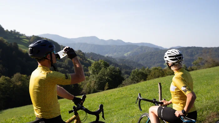 Two cyclists in yellow gear taking a break with mountain view
