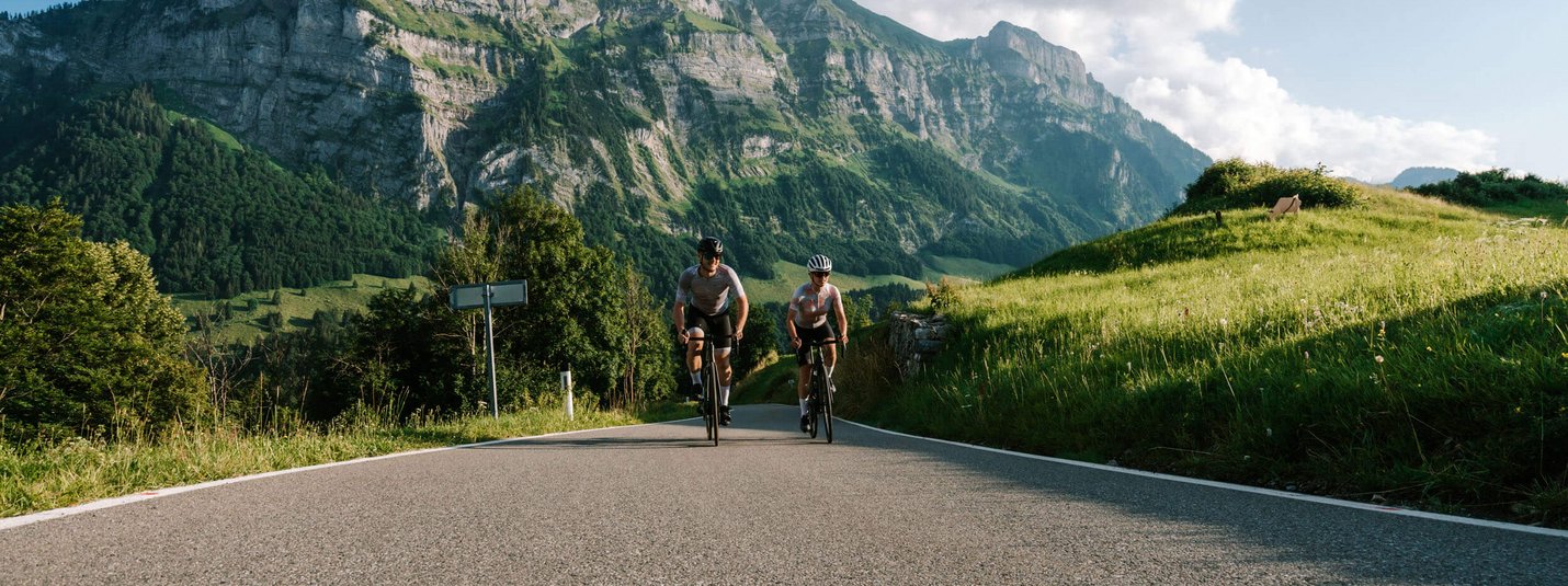 Twee fietsers op bergweg met rotsachtige kliffen en groene heuvels op de achtergrond