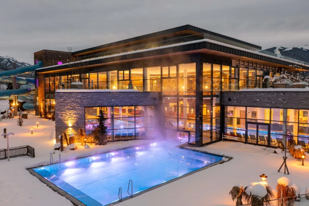 Hotel illuminato con piscina all’aperto in un paesaggio montano innevato al crepuscolo
