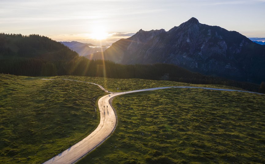 Sunset over winding mountain road with two cyclists and mountains in the background