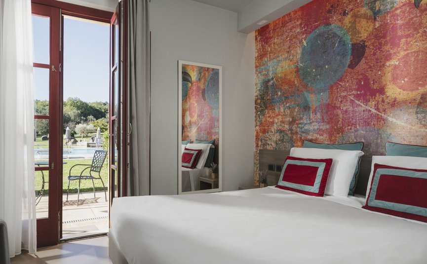 Hotel & Restaurant Casolare Le Terre Rosse ***S © Hotel Casolare Le Terre Rosse Modernes Schlafzimmer mit buntem Wandbild und Terrasse mit Blick auf einen Pool