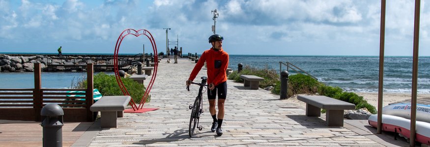 Cyclist walking with bike on a pier by the sea next to a heart decoration