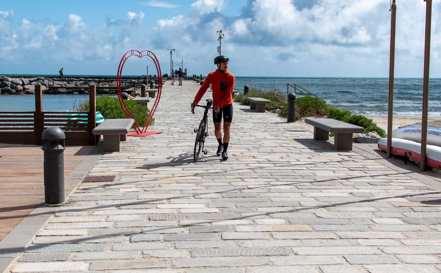 Cyclist walking with bike on a pier by the sea next to a heart decoration