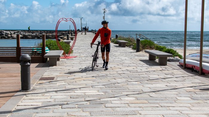Radfahrer geht mit Fahrrad auf einem Steg am Meer vorbei an einer Herz-Dekoration
