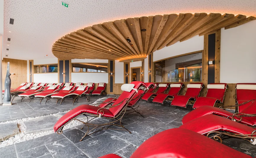 Ontspanningsruimte met rode ligstoelen en houten plafond in moderne spa