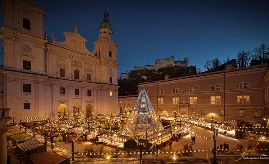Kerstmarkt met verlichte kraampjes naast de Dom van Salzburg en de vesting Hohensalzburg erboven