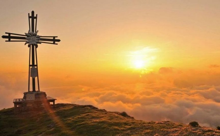 Wooden cross on mountain peak at sunrise above clouds