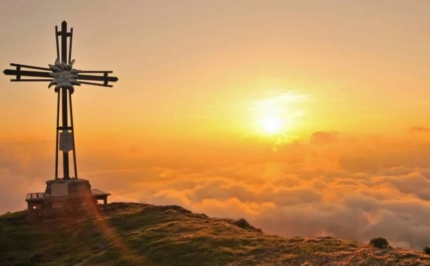 Kleine Kitzbühel Runde © Sportcamp Woferlgut Bruck Holzkreuz auf Berggipfel bei Sonnenaufgang über Wolken