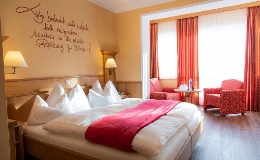 Cozy hotel room with double bed, red accents, and seating area near window