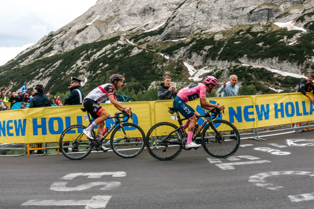 Due ciclisti in gara su strada di montagna davanti a spettatori