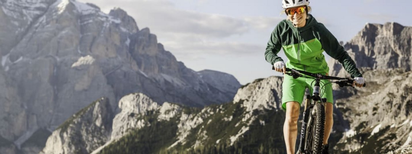 Woman mountain biking on rocky trail with mountains in the background