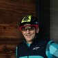 Uomo con casco da bici fa pollice su accanto a G illuminata su muro di legno