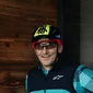 Mann in Fahrradhelm zeigt Daumen vor beleuchtetem G an Holzwand