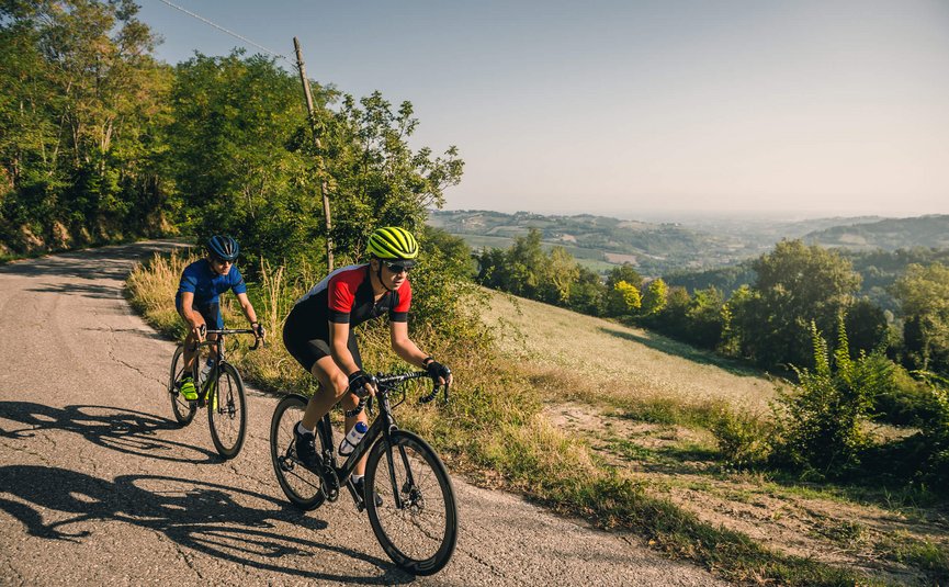Two cyclists riding on a country road through hilly countryside.