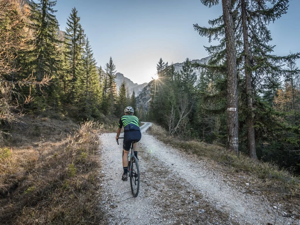 Fietser rijdt op bospaadje met zonsondergang en bergen op de achtergrond