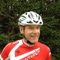 Man wearing white helmet and red cycling jersey by pine trees