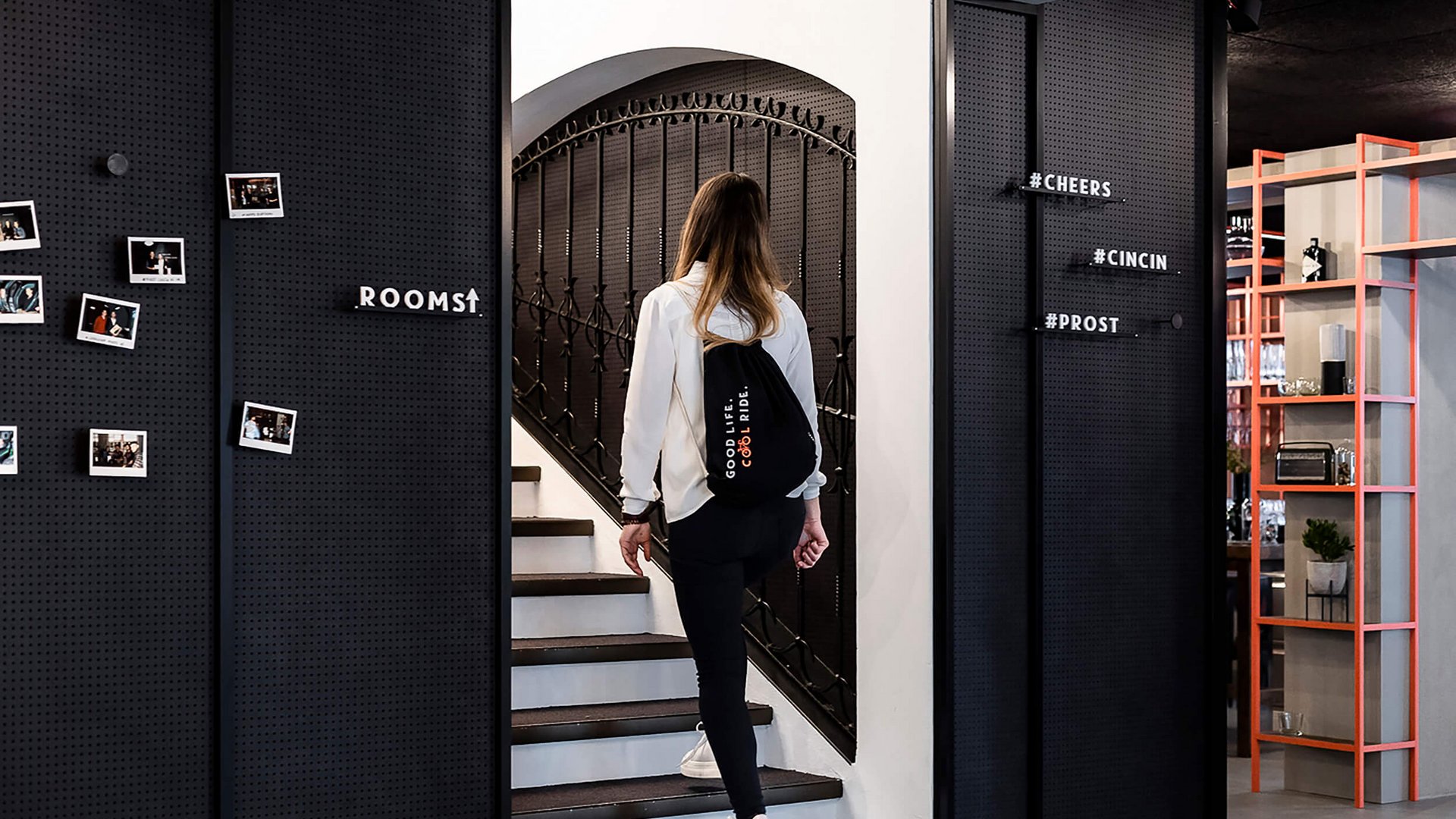 Frau mit Rucksack geht eine Treppe hinauf in modernem Innenraum