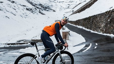 Radfahrer in Orangenweste auf nasser Bergstraße mit Schnee