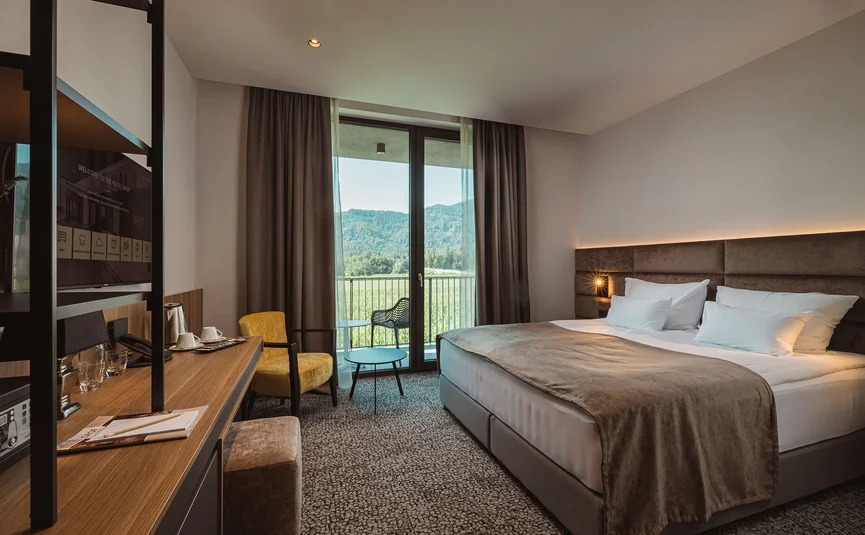 Modernes Hotelzimmer mit Doppelbett und Blick auf grüne Landschaft