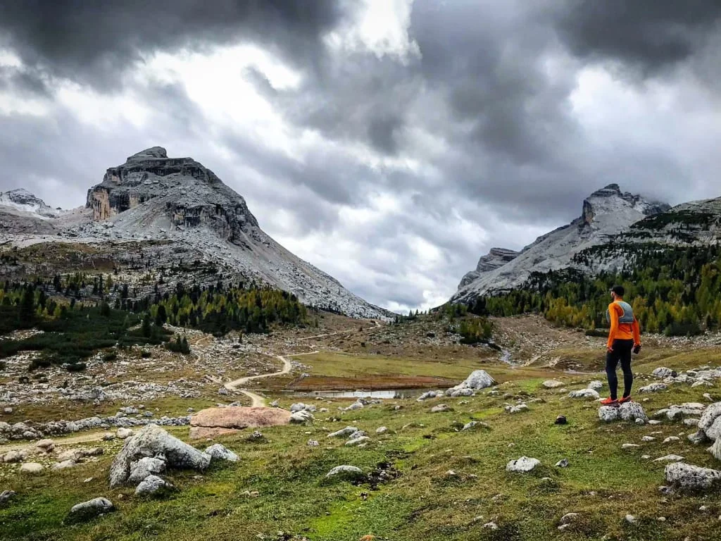 Wanderer in orange Jacke steht auf Felsen in bergiger Landschaft unter bewölktem Himmel