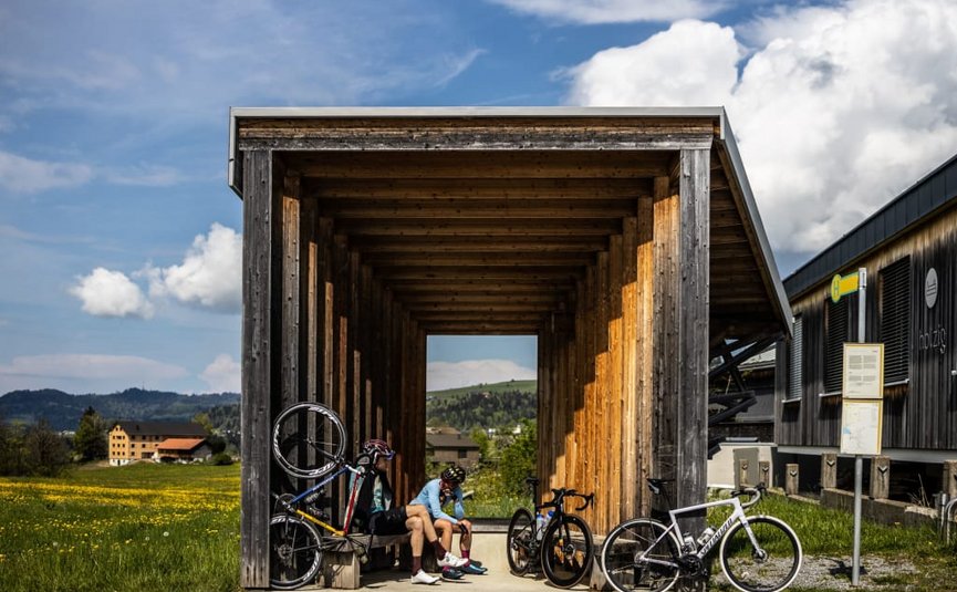 Pedal Punk Package Due ciclisti seduti in una struttura in legno accanto a una strada di campagna con le loro bici