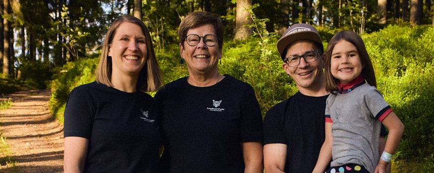 Vier Personen lächeln im Wald, Mann hält ein Mädchen auf dem Arm