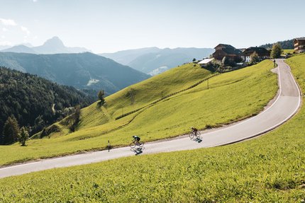 Twee fietsers op een kronkelende bergweg omgeven door groene heuvels