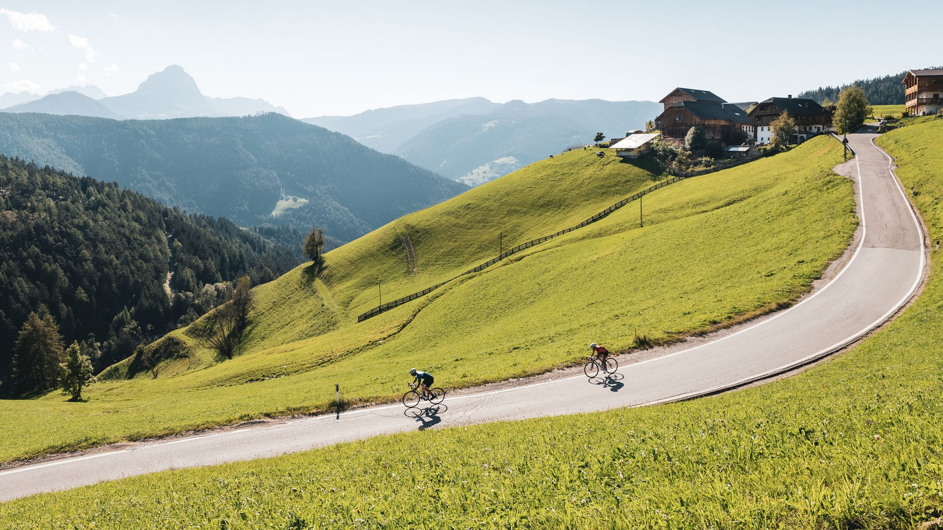 Zwei Radfahrer fahren eine kurvige Bergstraße umgeben von grünen Hügeln