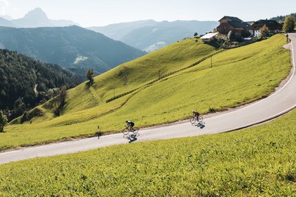 Twee fietsers op een kronkelende bergweg omgeven door groene heuvels