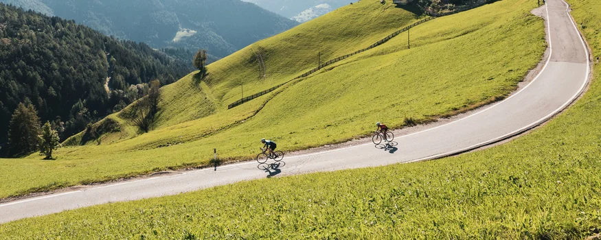 Twee fietsers op een kronkelende bergweg omgeven door groene heuvels