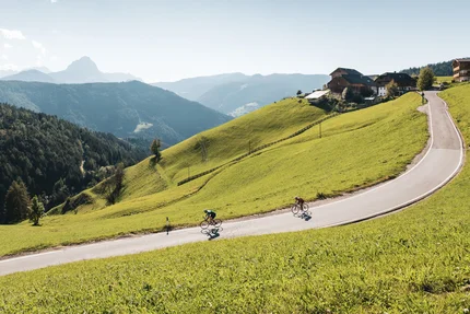 Twee fietsers op een kronkelende bergweg omgeven door groene heuvels