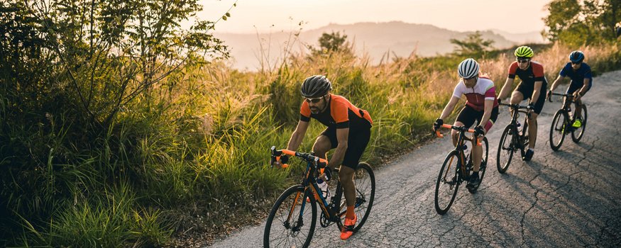 Vier Radfahrer fahren auf einer bergigen Landstraße bei Sonnenuntergang