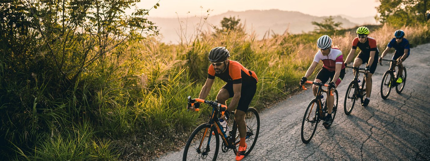 Quattro ciclisti su una strada di campagna in salita al tramonto