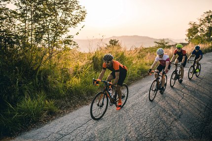 Four cyclists riding on a rural road uphill during sunset
