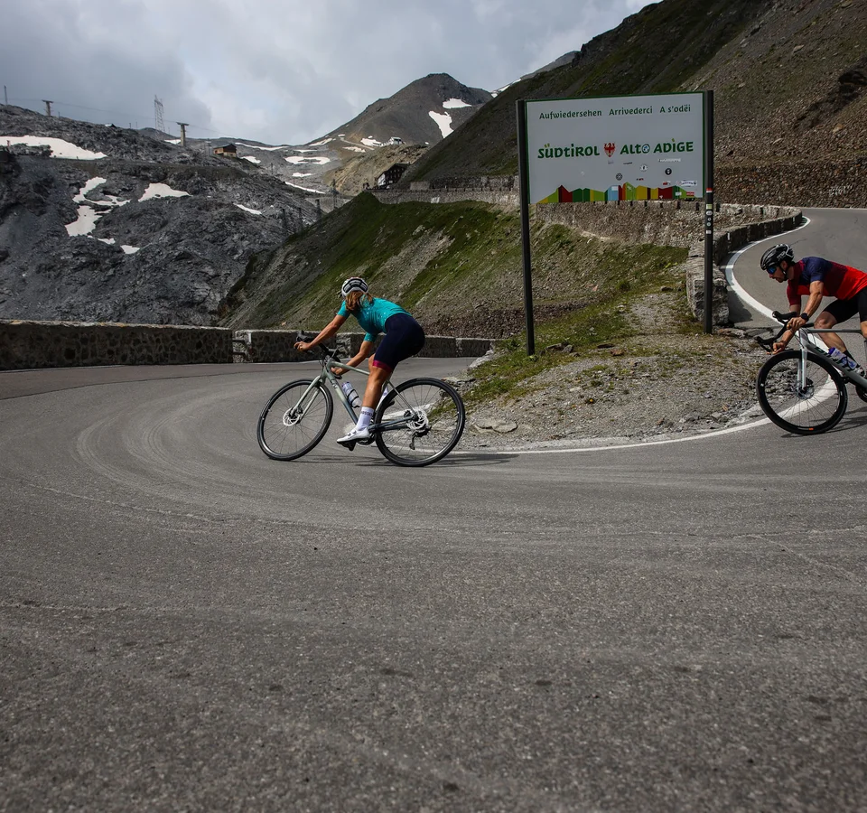 Zwei Radfahrer auf einer Bergstraße nahe einem Südtirol-Schild