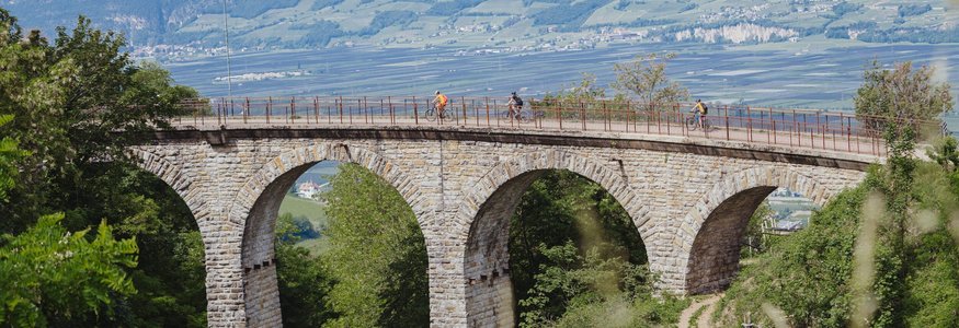 Fahrradfahrer auf einer Steinbrücke mit Bögen in einer grünen Landschaft