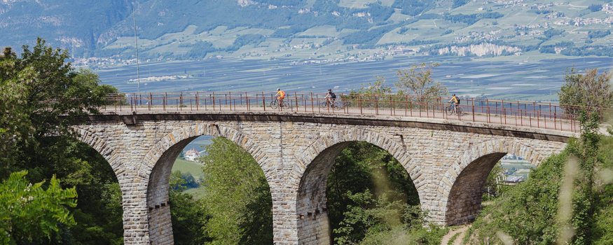 Fahrradfahrer auf einer Steinbrücke mit Bögen in einer grünen Landschaft