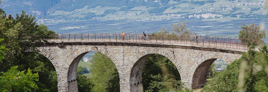 Fahrradfahrer auf einer Steinbrücke mit Bögen in einer grünen Landschaft