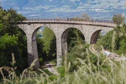 Fahrradfahrer auf einer Steinbrücke mit Bögen in einer grünen Landschaft