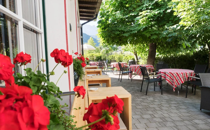 Zonnig terras buiten met tafels, stoelen en rode bloemen bij een restaurant