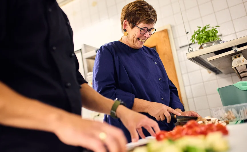 Vrouw snijdt groenten in professionele keuken, glimlachend en gefocust
