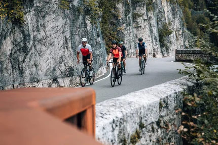 Vier Radfahrer fahren auf bergiger Straße entlang einer Felswand